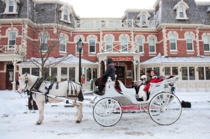 A couple riding in a horse drawn carriage outside of the Prince of Wales hotel.