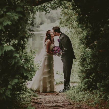 Bride and groom kissing in front of the mill pond at Millcroft Inn & Spa