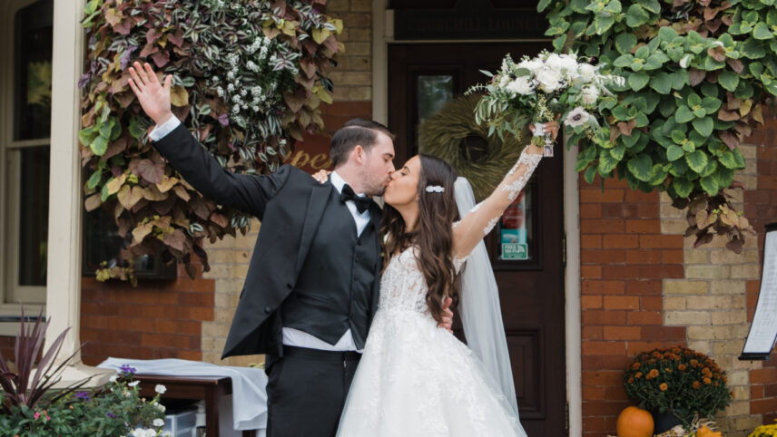 Bride and groom kissing outside the entrance to Prince of Wales