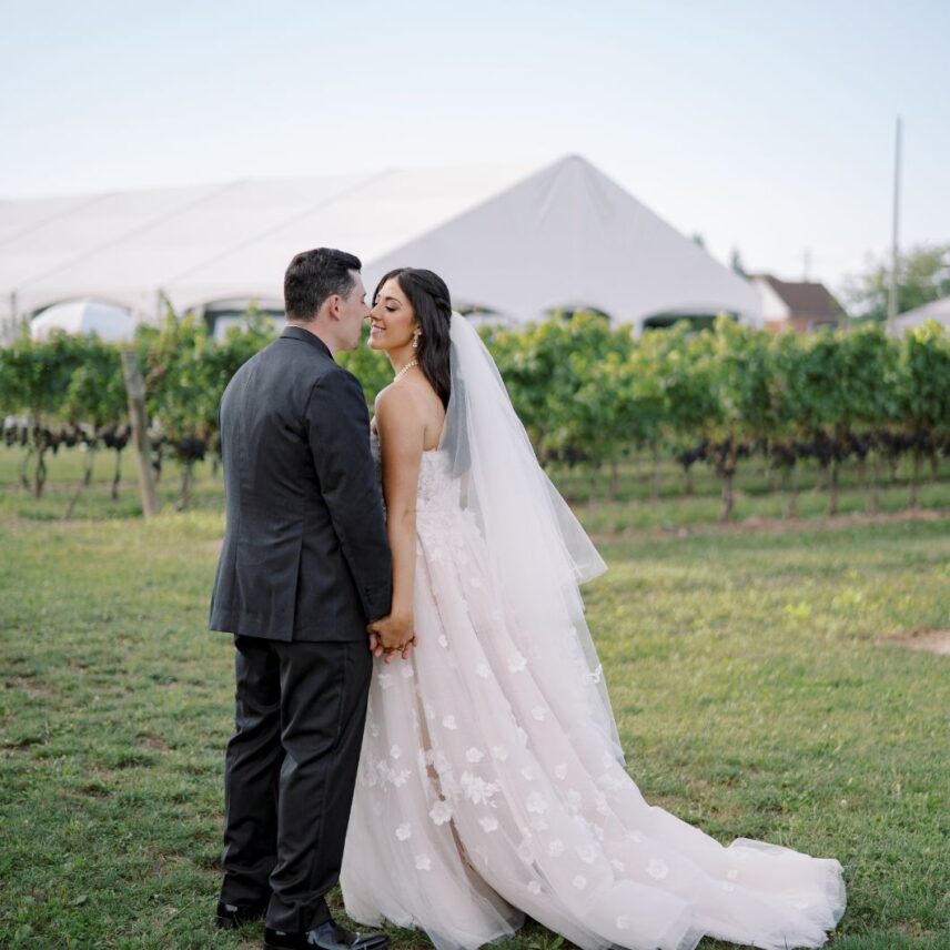 A couple kisses outside of Bella Terra Vineyards tented terrace a summer wedding venue