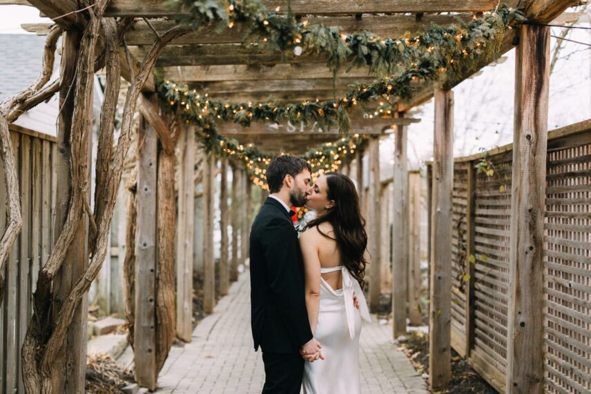 Bride and groom standing in festive Jordan Village surrounded by winter garlands and holiday lights