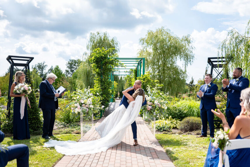 Large outdoor wedding ceremony at Pont de Monet in Niagara-on-the-Lake with a green Japanese bridge, pond, and waterfall