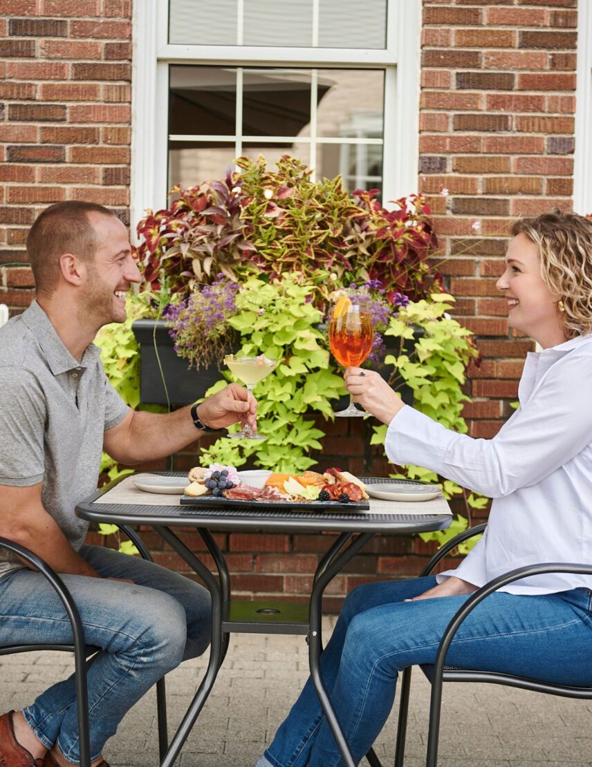 A couple celebrates with cocktails and charcuterie on the Inn On The Twenty Restaurant patio in Jordan Village
